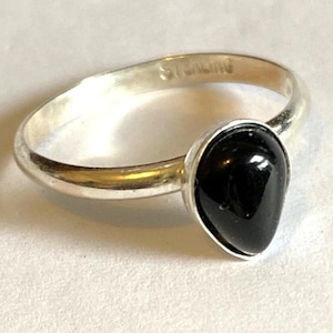 Peut inclure: Une bague en argent avec une pierre précieuse noire en forme de larme. La bague est marquée "Sterling" à l'intérieur de la bande.