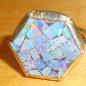 Puede incluir: Un anillo de plata con un engaste hexagonal que presenta un mosaico de piezas de ópalo iridiscente.