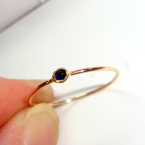 May include: A delicate gold ring with a single, small, dark blue gemstone.