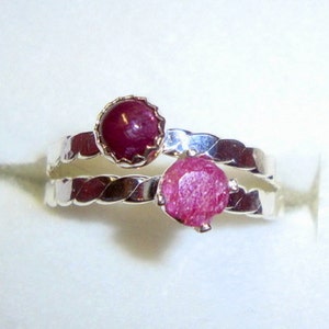 May include: A silver ring with two pink ruby stones. The ring has a braided band.