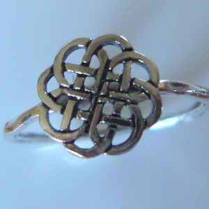 Puede incluir: Un anillo de plata con un diseño de nudo celta. El nudo es intrincado y detallado, y el anillo es simple y elegante.