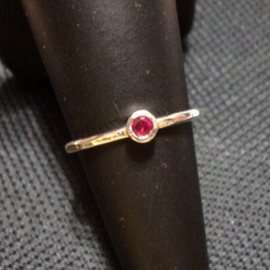 Puede incluir: Un anillo de plata con una sola piedra preciosa redonda, pequeña y roja.