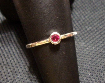Könnte beinhalten: Ein silberner Ring mit einem einzigen, kleinen, runden, roten Edelstein.