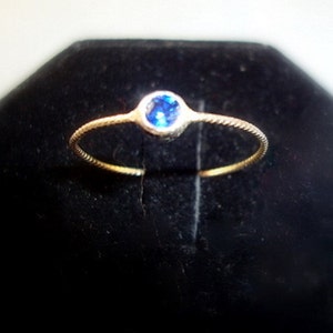 May include: A delicate gold ring with a small, round blue gemstone.