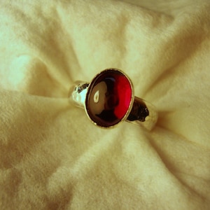 Peut inclure: Une bague en argent avec une pierre précieuse rouge sertie dans un sertissage à bélière. La bague a une texture martelée.