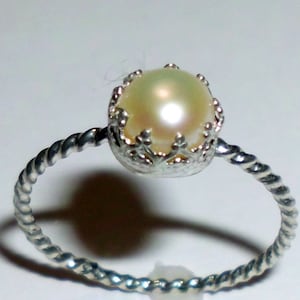 May include: A silver ring with a twisted band and a pearl set in a crown-shaped setting.