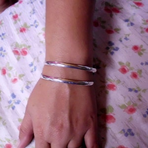 May include: A silver bangle bracelet with a polished finish. The bracelet is worn on a person's wrist.