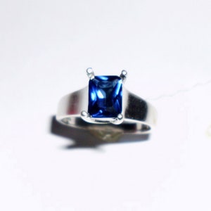 May include: A silver ring with a square-shaped blue gemstone.