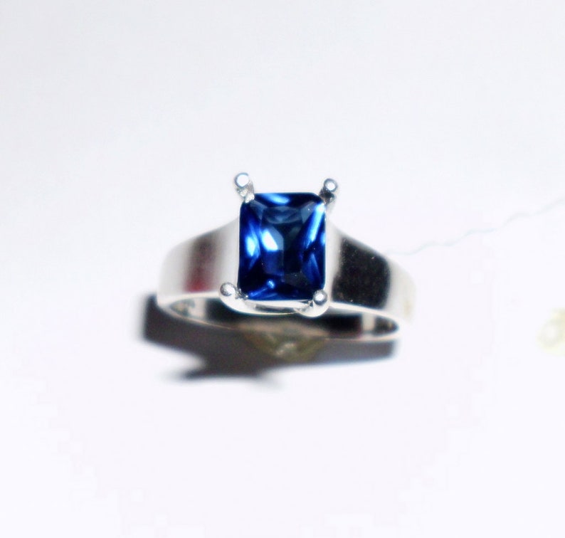 May include: A silver ring with a square-shaped blue gemstone.
