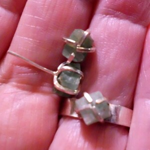 May include: Three green gemstone earrings with silver wire settings. The earrings are shown on a finger.