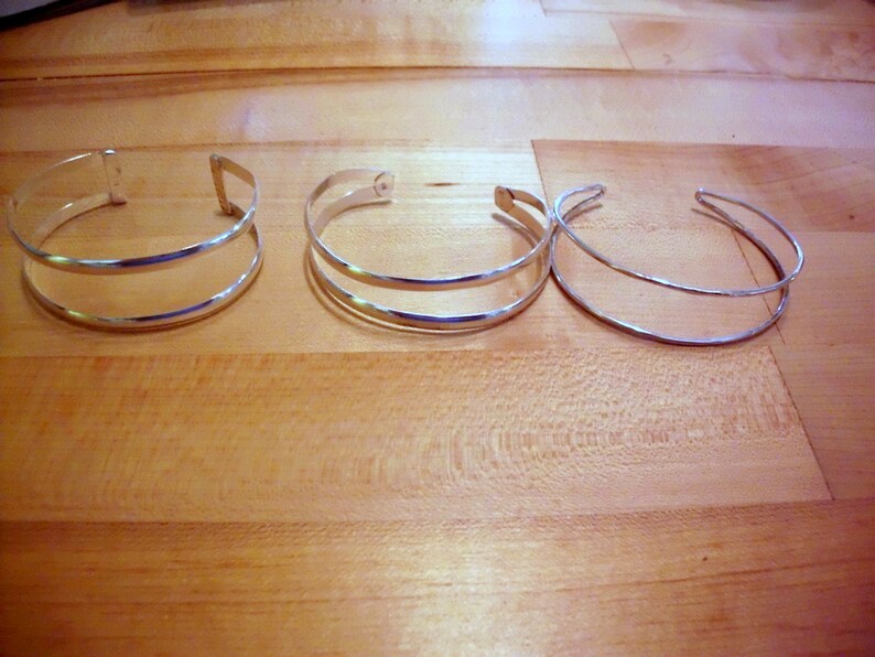 May include: Three silver bracelets, two with a double band design and one with a single band.