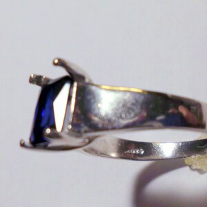 May include: A silver ring with a large, dark blue square-shaped gemstone set in a prong setting.