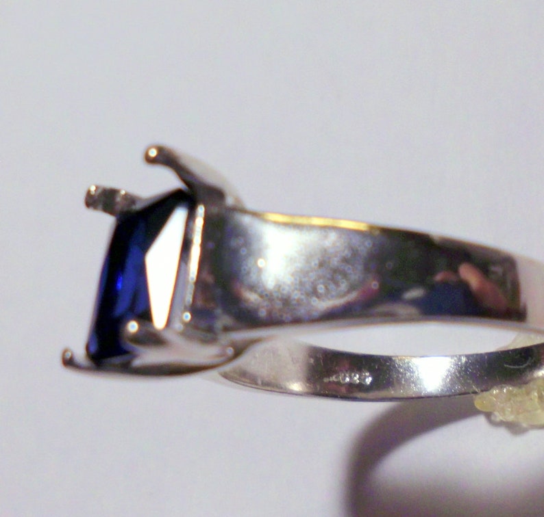 May include: A silver ring with a large, dark blue square-shaped gemstone set in a prong setting.