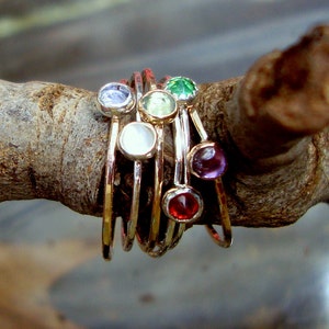 May include: A set of seven gold rings with colourful gemstones. The rings are stacked on top of each other and are arranged in a circle. The gemstones are a variety of colours, including purple, red, green, white, and blue.