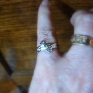 May include: A silver ring with two stones, one blue and one clear, set in a unique design.