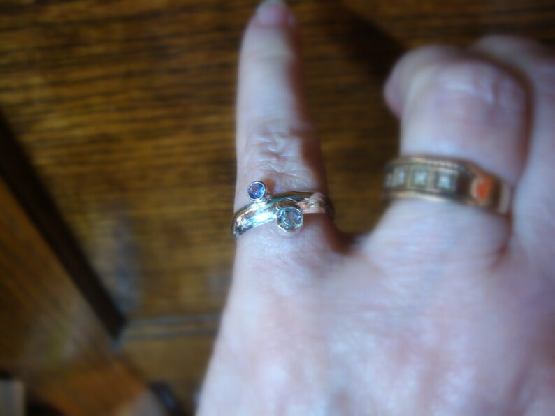 May include: A silver ring with two stones, one blue and one clear, set in a unique design.