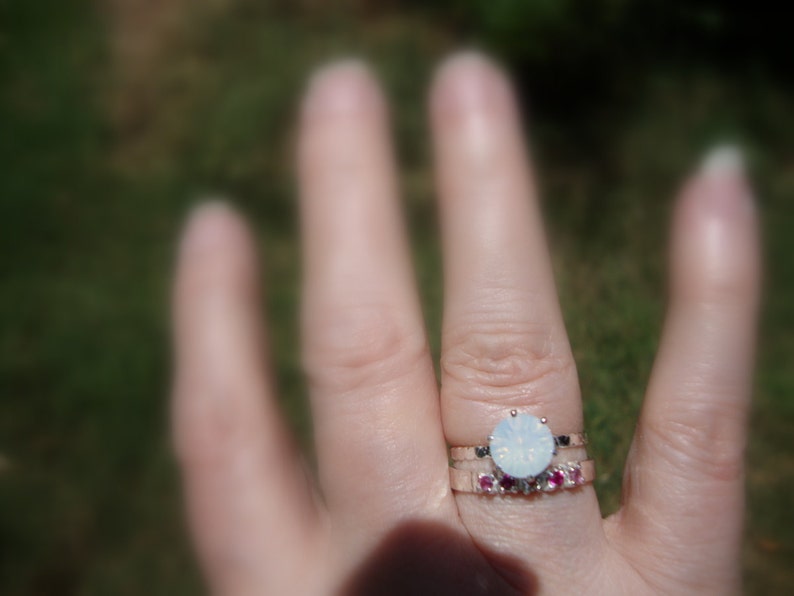 May include: A silver ring with a large, round, white opal stone. A smaller band with pink stones sits below the opal ring.