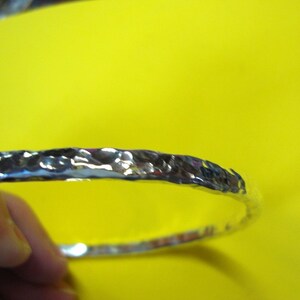 Puede incluir: Un brazalete de plata martillado. El brazalete es liso y brillante, con una superficie texturizada.