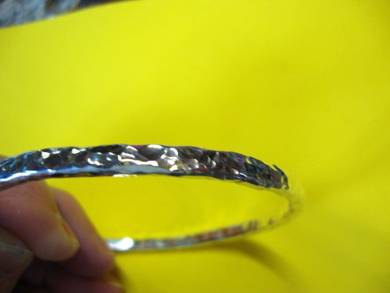 Puede incluir: Un brazalete de plata martillado. El brazalete es liso y brillante, con una superficie texturizada.