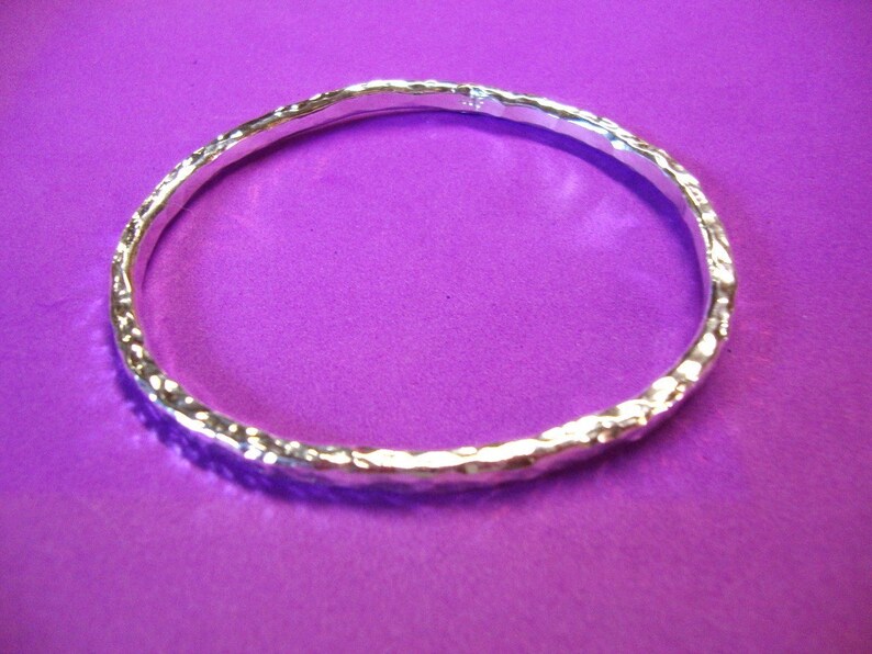 Puede incluir: Un brazalete de plata con textura martillada. El brazalete est&aacute; sobre un fondo morado.