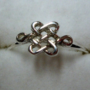 Puede incluir: Un anillo de plata con un diseño de nudo. El nudo es un símbolo tradicional de buena suerte y eternidad.