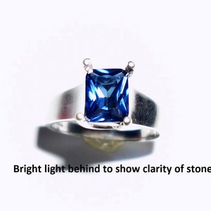 May include: A silver ring with a large, square-shaped, blue sapphire gemstone.