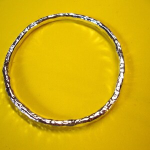 Puede incluir: Un brazalete de plata con textura martillada. El brazalete est&aacute; sobre un fondo amarillo.