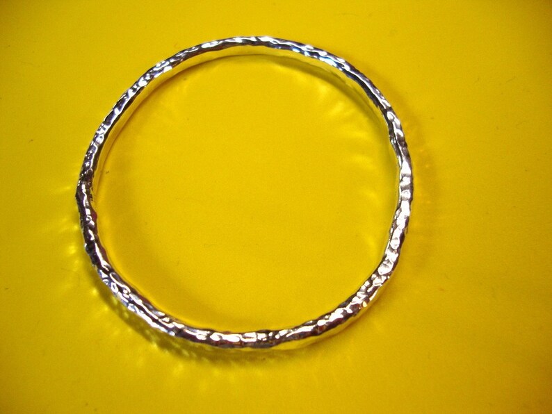 Puede incluir: Un brazalete de plata con textura martillada. El brazalete est&aacute; sobre un fondo amarillo.