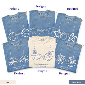 May include: A collection of blue jean and ivory t-shirts with various white graphic designs. Designs include seashells, bikini tops, starfish, flowers, and coconuts. Each shirt has a gold necklace and text that reads "Cassandra's bachelorette Key West, 2016."