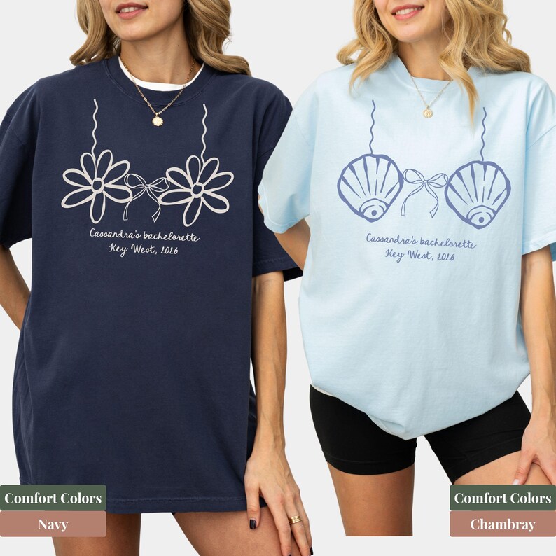 May include: Two t-shirts, one navy and one chambray, featuring a graphic design of a floral bra and seashell bra, respectively. The text "Cassandra's bachelorette Key West, 2016" is printed below the designs. The bottom of the image shows the color names.