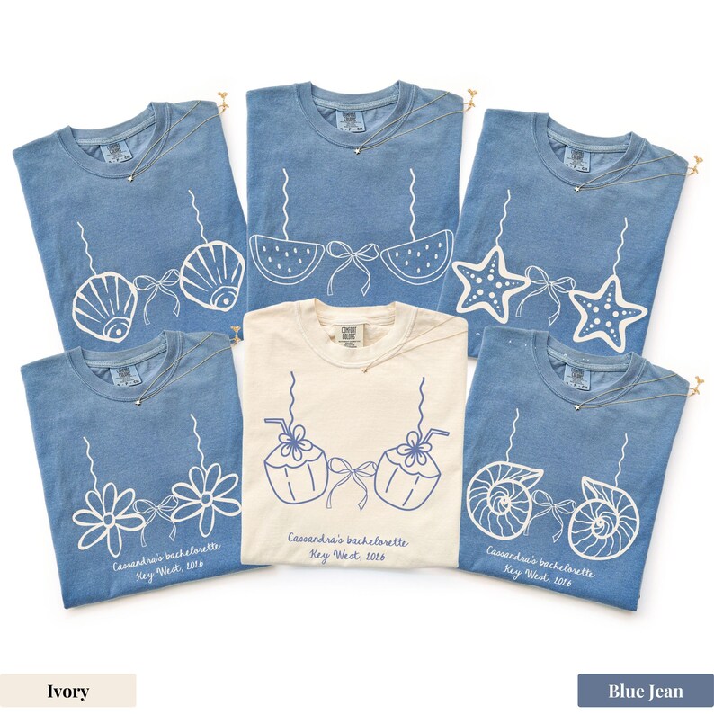 May include: A collection of blue jean and ivory t-shirts with various white graphic designs, including seashells, starfish, and flowers. Each shirt has a necklace and the text "Cassandra's bachelorette Key West, 2016".