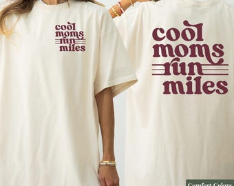 Könnte beinhalten: Ein elfenbeinfarbenes Kurzarm-T-Shirt mit dem kastanienbraunen Schriftzug "cool moms run miles" in einer Retro-Schriftart auf der linken Brust und in größerer Ausführung auf dem Rücken, akzentuiert durch horizontale Linien.