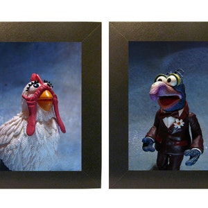 Puede incluir: Dos imágenes enmarcadas, una con una figurita de pollo blanca con un pico y cresta rojos, y la otra con una figurita de Muppet azul y morado con un esmoquin y una flor blanca.