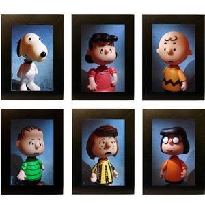 Pode incluir: Um conjunto de seis imagens emolduradas com personagens da tira de quadrinhos Peanuts. Os personagens são Charlie Brown, Lucy, Linus, Snoopy, Sally e Peppermint Patty. Cada imagem está em uma moldura preta com um passe-partout branco.