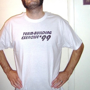 May include: White t-shirt with the text "TEAM-BUILDING EXERCISE '99" printed in black.