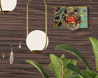 Op de afbeelding: Twee gouden hanglampen met witte bolvormige lampenkappen hangen aan een donkerhouten plafond. Een klein abstract schilderij met blauwe, groene en rode kleuren hangt aan de muur achter de lampen. Een groene, bladerrijke plant staat op een houten oppervlak op de voorgrond.
