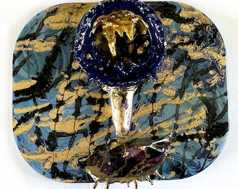 Op de afbeelding: Een abstract beeldhouwwerk in blauw en goud met een getextureerd oppervlak. Het beeldhouwwerk is gemonteerd op een blauwe en gouden achtergrond.