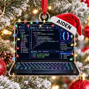 May include: A rectangular acrylic ornament shaped like a laptop computer, featuring a screen displaying code, a keyboard, and a string of colorful Christmas lights around the frame. A red Santa hat with the name AIDEN printed on the white trim is attached.