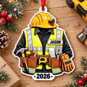 May include: A decorative ornament shaped like a construction worker's uniform, featuring a yellow hard hat, a black shirt, and a high-visibility yellow vest with reflective strips. It includes a brown tool belt with a hammer, pencil, tape measure, and wrench, with the name JASON and the year 2026 printed on it.