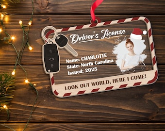 May include: A wooden ornament shaped like a driver's license, featuring a photo of a person wearing a Santa hat. The ornament includes the text "Driver's License," the name "CHARLOTTE," and the state "North Carolina." It also has the text "LOOK OUT WORLD, HERE I COME!"