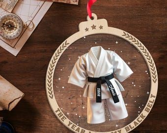 May include: Wooden ornament with a karate uniform design. The ornament features a white karate uniform with a black belt. The belt has the year 2025 and the name "Annie" printed on it. The text "THE YEAR I GOT MY BLACK BELT" is printed on the ornament.