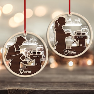 May include: Two wooden coffee-themed ornaments with red hanging ribbons. Each ornament features a barista silhouette, coffee machine, and the year 2025. One ornament is labeled "David," the other "Olivia."