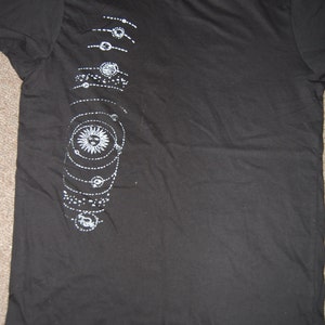 May include: Black t-shirt with a white graphic of a sun and planets on the left side. The shirt has a crew neck and short sleeves. The size tag says "L" and "Urban Outfitters".