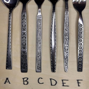 May include: Close-up of six silver spoons and forks with different decorative patterns. The spoons and forks are arranged in a row from left to right, labeled A through F.