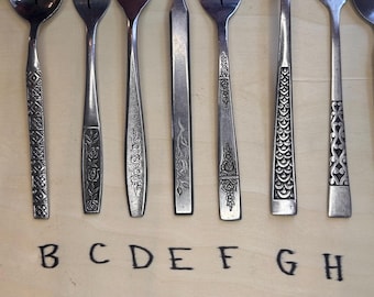 May include: Nine silver spoons with different decorative patterns on the handles. The spoons are labelled A through I.