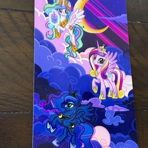 May include: A rectangular sticker featuring three cartoon ponies against a purple and blue night sky background. The top pony has a golden crown and a drink. The middle pony is pink and purple. The bottom pony is dark blue with a crescent moon.