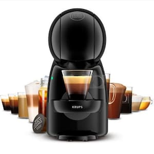 Pode incluir: Uma máquina de café Krups Dolce Gusto preta com um copo de café em camadas no centro. Várias bebidas de café estão dispostas atrás da máquina. Uma cápsula de café Dolce Gusto está em frente à máquina.