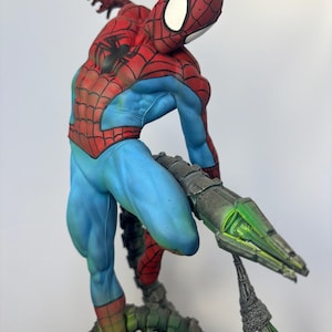 May include: A detailed figurine of Spider-Man in a dynamic pose, featuring a red and blue costume with web detailing. The figure is supported by a metallic, green-lit structure, showcasing intricate design and vibrant colors.