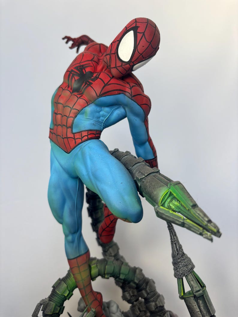 May include: A detailed figurine of Spider-Man in a dynamic pose, featuring a red and blue costume with web detailing. The figure is supported by a metallic, green-lit structure, showcasing intricate design and vibrant colors.