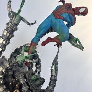 May include: A dynamic action figure of Spider-Man in a blue and red suit, posed mid-air, battling against Doctor Octopus's mechanical arms. The arms are metallic gray and green, with intricate details. The figure is set against a white background.